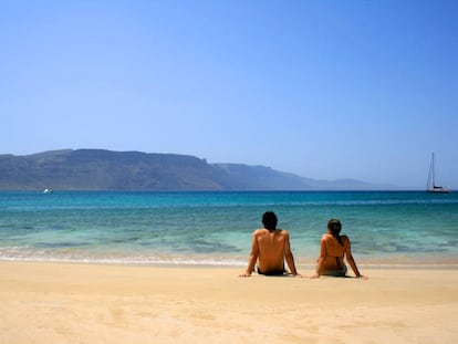 Una pareja sentada en una playa de la isla de La Graciosa (Canarias).