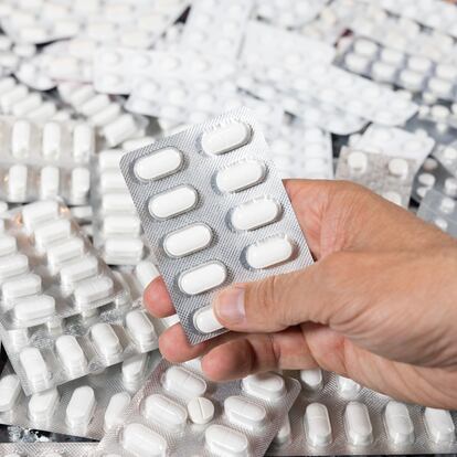 Man's hand holding a package of encapsulated pills. There is a large number of pills