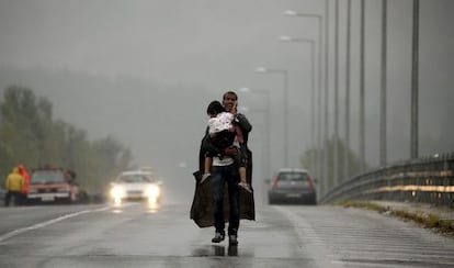 Un refugiado grita a sus compañeros que le esperen, mientras camina con su hija en brazos por una carretera griega hacia Macedonia.