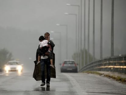 Um refugiado grita a seus companheiros para que esperem, enquanto caminha com sua filha no colo por uma estrada grega para a Macedônia.