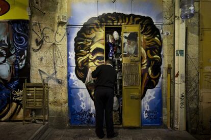 Un comerciante cierra las puertas de su establecimiento en el mercado Mahane Yehuda, decorado con un grafiti del artista callejero Solomon Souza, en Jerusalén (Israel).