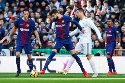 El defensa del FC Barcelona, Gerard Piqué, intenta controlar el balón ante el delantero portugués del Real Madrid, Cristiano Ronaldo, y en presencia de su compañero, Sergio Busquets.