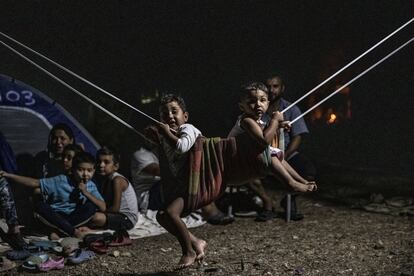 Cae la noche en Lesbos y la carretera de Moria es un hervidero de figuras humanas que sortean escombros y camiones. En la imagen, un grupo de niños y adultos, junto al campo de refugiados de Moria.