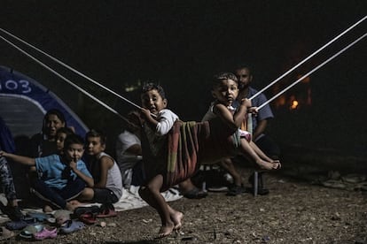 Cae la noche en Lesbos y la carretera de Moria es un hervidero de figuras humanas que sortean escombros y camiones. En la imagen, un grupo de niños y adultos, junto al campo de refugiados de Moria.