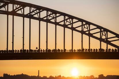 Varias personas cruzan un puente sobre el río Waal durante el primer día de la 100 edición de la Cuádruple Marcha Internacional de Nijmegen, Holanda. Este evento anual, que se celebra desde 1909, reúne a numerosos participantes que realizan marchas diarias de hasta 50 km durante cuatro jornadas.