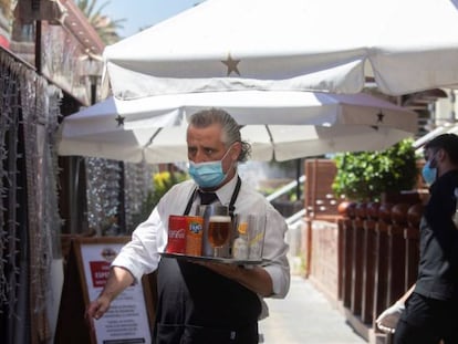 Un camarero lleva su pedido a unos clientes a una de las terrazas del Puerto Olímpico de Barcelona.