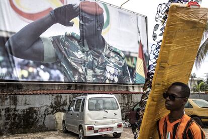Un vendedor de gafas de sol pasa delante de un gran cartel donde aparece el teniente coronel Mamady Doumbouya, este 11 de septiembre en Conakry.