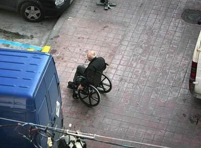 Una persona en silla de ruedas sortea vehículos en una acera de Valencia.