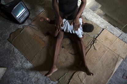 Loavia Bienaimé, consuela a su hija menor, Martina, mientras ven la televisión en el hueco de la escalera, fuera de su habitación en un edificio abandonado del Gobierno haitiano.