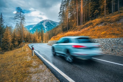 Un coche gris circula por una carretera entre montañas.