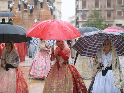 Falleras desfilan en Valencia durante la ofrenda y se protegen con paraguas de la lluvia.