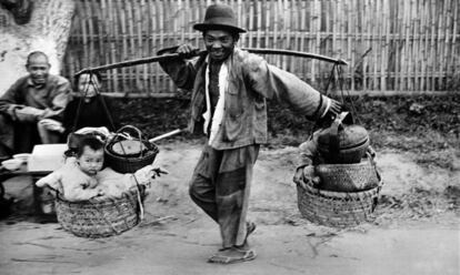1946, Birmania. Un refugiado lleva a los niños y sus enseres metidos en cestas en una calle de la ciudad de Mandalay.