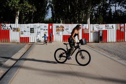 Una mujer pasa junto a unos carteles colocados por los vecinos del distrito de Arganzuela , a manera de protesta, en una de las vallas puestas en el parque Madrid Río, donde se proyecta una de las estaciones de metro de la ampliación de la línea 11, el 27 de septiembre de 2023.