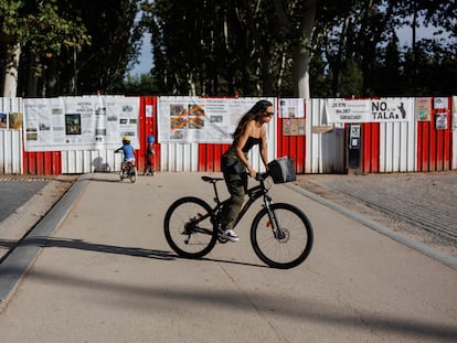 Una mujer pasa junto a unos carteles colocados por los vecinos del distrito de Arganzuela , a manera de protesta, en una de las vallas puestas en el parque Madrid Río, donde se proyecta una de las estaciones de metro de la ampliación de la línea 11, el 27 de septiembre de 2023.