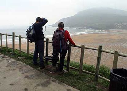 Dos peregrinos disfrutan con la vista de la playa de La Arena, en Zierbena (Vizcaya), en un tramo del Camino del Norte que discurre en este punto por una antigua vía de ferrocarril reconvertida en senda.