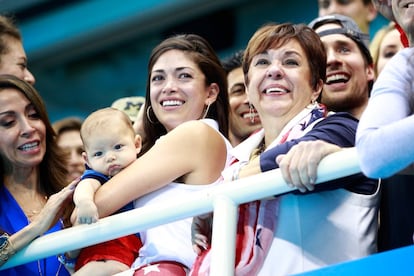 Nicole Johnson, la prometida de Michael Phelps, sostiene en brazos a Boomer, el hijo de ambos, mientras la madre del nadador, Debbie Phelps, llora al ver a su hijo colgarse la medalla de oro en la que es su última competición olímpica.