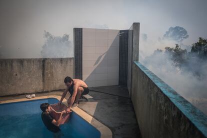 Dos vecinos de Caneças sacan agua de una piscina para intentar sofocar el fuego que amenaza sus viviendas, este pasado domingo. 