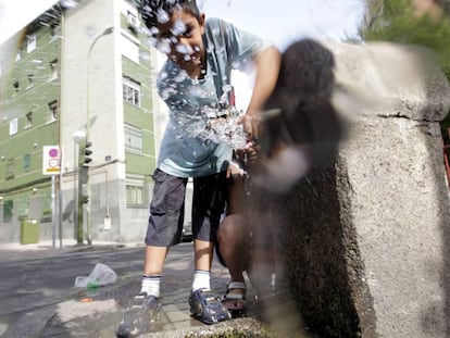 Un ni&ntilde;o juega con el agua de una fuente en el barrio de San Blas, Madrid. 