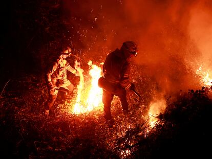 Dos bomberos trabajan esta pasada noche en la extinción de un incendio en Piedrafita, en Asturias.