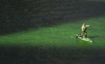 Un surfero con su tabla de paddle surf navega por las aguas del río Chicago teñidas de verde durante la conmemoración del día de San Patricio.