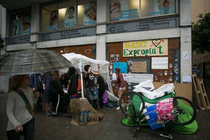 Activistas soportan la lluvia baja la mirada de los vecinos frente al Banc Expropiat.