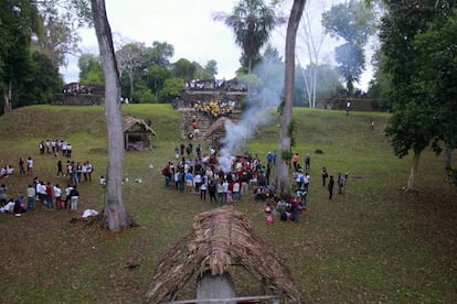 Un grupo de guías espirituales mayas realizan una ceremonia de fuego mientras varios turistas trepan estructuras arqueológicas de más de 2.000 años de antigüedad, en Uaxactún.