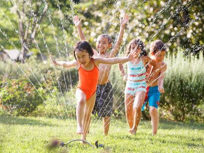 Varios niños juegan y se mojan con los aspersores de un jardín.