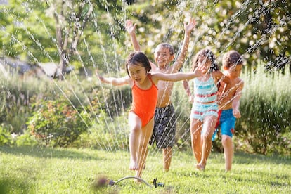 Varios niños juegan y se mojan con los aspersores de un jardín.