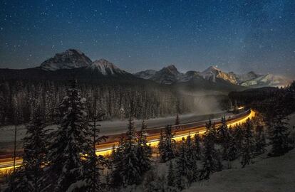 Tren de carga que pasa por la famosa "Curva de Morant", hermosa vista del río Bow helado en el parque nacional de Banff cerca del lago Louise, Canadá..