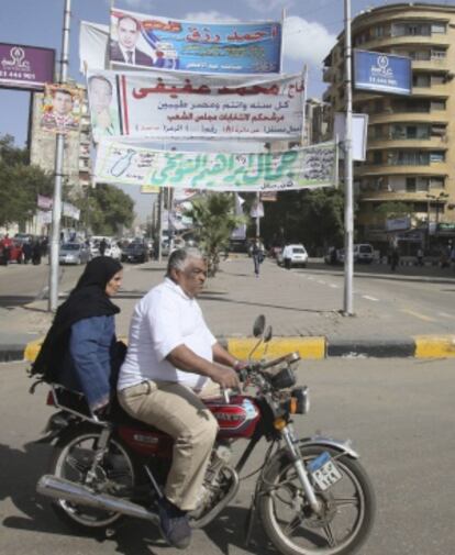 Una pareja circula en moto por una calle decorada con pancartas y carteles electorales, en El Cairo.