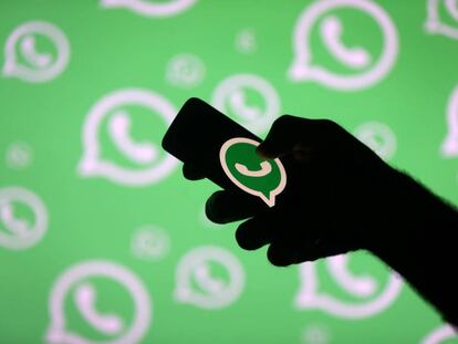 Un hombre con un móvil posa frente a una pantalla con el logo de WhatsApp.
 