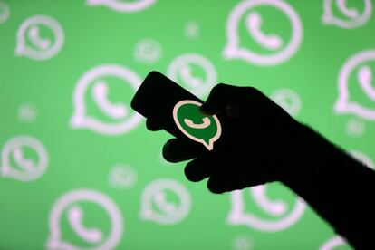 Un hombre con un móvil posa frente a una pantalla con el logo de WhatsApp.