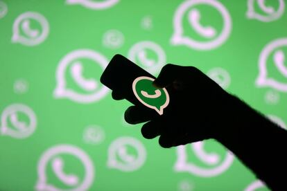 Um homem com um móvel posa em frente a uma tela com o logotipo de WhatsApp.