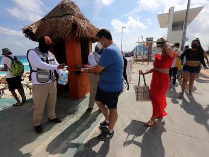 Un hombre reparte líquido desinfectante a turistas en la playa en Cancún, en enero.