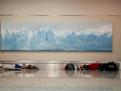 Homeless men sleep below a photo of the Perito Moreno Glacier at the Jorge Newbery international airport in Buenos Aires, Argentina, Thursday, April 6, 2023.