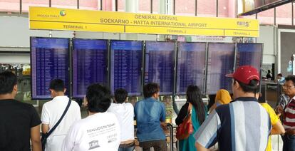 Varios pasajeros consultan los detalles de sus vuelos en una pantalla en un aeropuerto