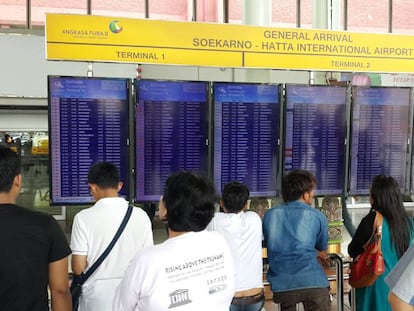 Varios pasajeros consultan los detalles de sus vuelos en una pantalla en un aeropuerto