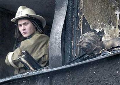 Un bombero mira por una ventana de la residencia universitaria incendiada en Moscú, junto a otra en la que aparece el cadáver calcinado de un estudiante