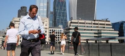 Un hombre utiliza su teléfono móvil, mientras que una mujer toma una fotografía con su smartphone en el London Bridge de la capital británica.