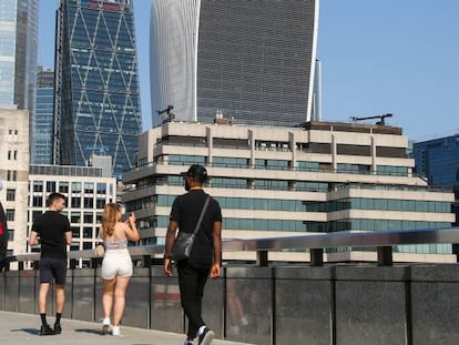 Un hombre utiliza su teléfono móvil, mientras que una mujer toma una fotografía con su smartphone en el London Bridge de la capital británica. 