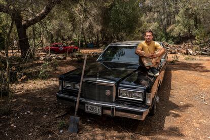 Liam Aldous, director creativo de ColourFeel, en la casa que está restaurando con otras personas en el interior de la isla de Ibiza. En la foto posa con uno de los coches antiguos que tienen en el terreno. 