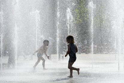 Dos ni&ntilde;os juegan con el agua de una fuente en Suiza.