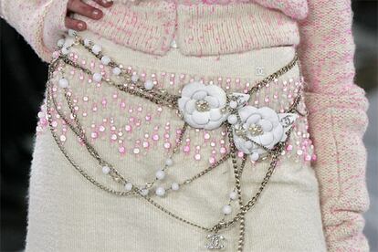 Para las nieves de 2006, Lagerfeld propone no olvidar la primavera. Así, este conjunto de lana beige y rosa se completa con un iamginativo cinturón de cadenas plateadas y perlas de imitación con dos rosas de tela blanca, todo ello sobre una base de lentejuelas de reflejos fucsias.