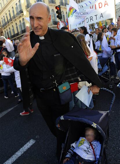 Un cura, participante en la protesta, se apoya en el carro de un bebé.