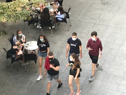 Varios jóvenes paseando con mascarilla delante de una terraza.