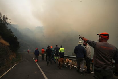 Vecinos esperan para bajar a refrescar la zona e impedir el avance del fuego hacia Santo tirso en la carretera desde Santo Tirso de Cabarcos a Oencia en Ponferrada (León), este lunes.