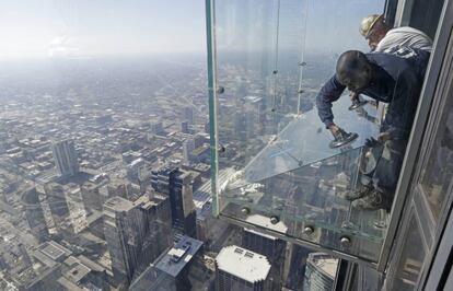 Trabajadores de una empresa de cristales reemplazan una capa protectora de un cristal instalado en el suelo que sobresale del piso 103 de la Torre Sears en Chicago (EE UU).