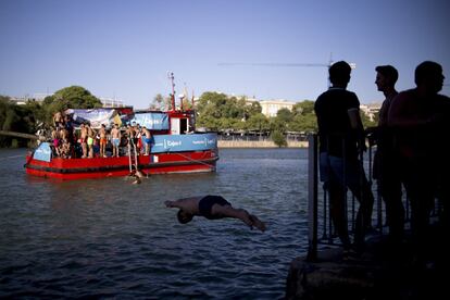 La tradición más divertida de la Velá de Santa Ana congregó a decenas de participantes en la zapata del Guadalquivir con el objetivo de conseguir una de las cinco banderas del día. En la imagen, varios jóvenes se zambullen en las aguas del Guadalquivir para participar en la cucaña, en el barrio sevillano de Triana.