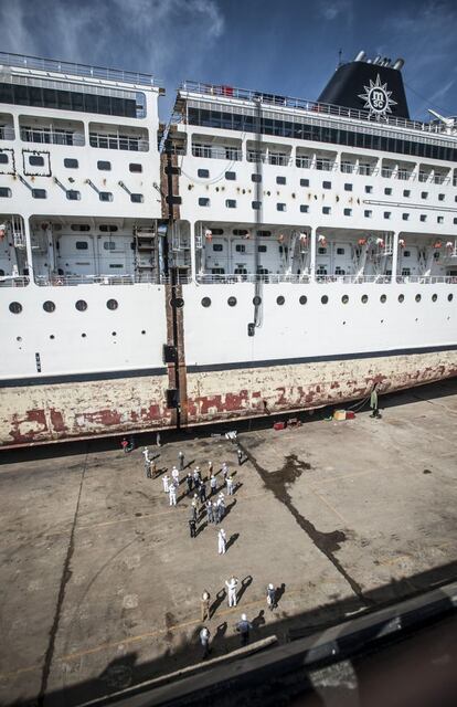 En el dique seco del astillero, el barco ha sido partido por la mitad como si de una barra de pan se tratase. En la imagen, ingenieros y técnicos observan la línea de corte.