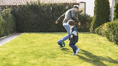 Un padre y un niño juegan a la pelota sobre un césped en buen estado.